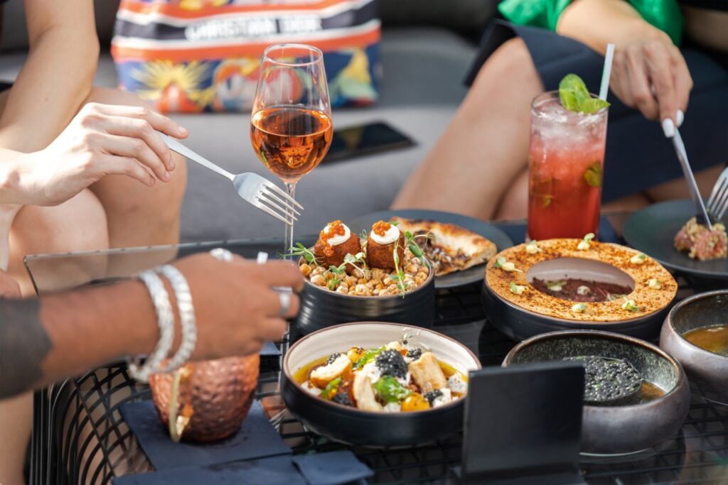 Eating out - a photograph of a table laid out with food and drink, with the hands of people enjoying it.