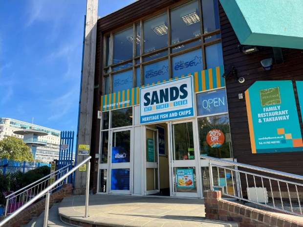 The glass frontage of "Sands by the Sea" with a sign saying "Heritage Fish and Chips".