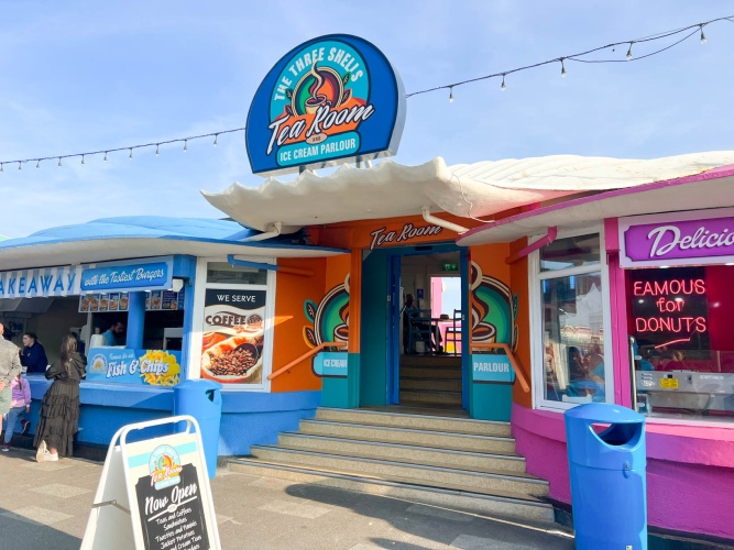 Exterior of the Three Shells Beach Café Sealife Adventure. A tea room and ice cream parlour accessed up a short flight of steps between two takeaway outlets.